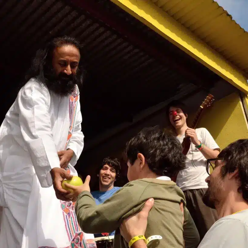 Gurudev passes an apple to a small child while on stage in Retiro