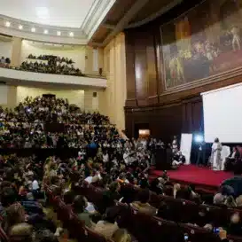 Gurudev speaks to a crowd inside an auditorium