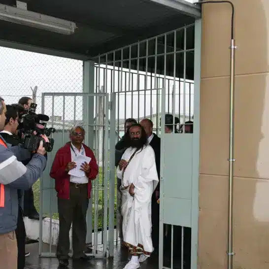 Gurudev enters through prison gates while reporters and camera men capture the moment